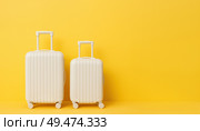 Two white hard shell suitcases with handles on wheels standing against yellow background, symbol of holiday, travel, trip, tourism, adventure. Стоковое AI-изображение, AI-художник Павел Муравьев / Фотобанк Лори