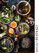 Top view of Asian food dishes. Asian noodle soup preparation on dark rustic kitchen table. Pot with stock, cooked noodles, various vegetables and meatballs. Meatball noodle soup in bowl with chopstick. Стоковое фото, агентство Ingram Publishing / Фотобанк Лори