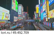 Osaka, Japan - Sep 22 2024, 4k, Panoramic view of Dotonbori river with a ship with tourists, a lot of people on embankment, there are a lot of advertising and illuminations on buildings, Osaka, Japan. Редакционное видео, видеограф Сергей Богомяко / Фотобанк Лори