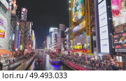 Osaka, Japan - Sep 22 2024, 4k, Panoramic view of Dotonbori river with a ship with tourists, a lot of people on embankment, there are a lot of advertising and illuminations on buildings, Osaka, Japan. Редакционное видео, видеограф Сергей Богомяко / Фотобанк Лори
