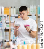 Attentive interested young guy client choosing between two boxes of paracetamol antipyretic pills in drug store. Стоковое фото, фотограф Яков Филимонов / Фотобанк Лори