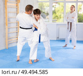 Judo or jiu-jitsu classes - two men practicing grabbing and throwing on sports mats under the guidance of trainer. Стоковое фото, фотограф Яков Филимонов / Фотобанк Лори