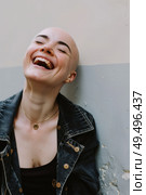 Charming bald woman stands against a wall, laughing heartily. She appears joyful and carefree as she enjoys a moment of levity. Стоковое AI-изображение, AI-художник Данила Большаков / Фотобанк Лори