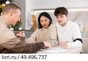 Male realtor discusses the terms of contract with couple in office of real estate agency, offering various accommodation options against backdrop of Christmas tree. Стоковое фото, фотограф Яков Филимонов / Фотобанк Лори