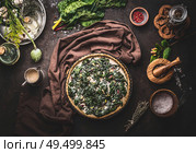 Quiche or open faced savory pie cooking preparation on dark rustic background with kitchen utensils and ingredients, top view. Tasty seasonal baking. Стоковое фото, агентство Ingram Publishing / Фотобанк Лори