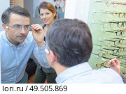 beautiful optician helping male customer choosing eye glasses. Стоковое фото, агентство Ingram Publishing / Фотобанк Лори