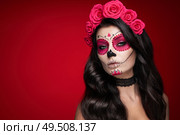 Portrait of a woman with sugar skull makeup over red background. Halloween costume and make-up. Portrait of Calavera Catrina. Стоковое фото, агентство Ingram Publishing / Фотобанк Лори