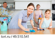 Cheerful woman wiping table in kitchen with preteen daughter. Стоковое фото, фотограф Яков Филимонов / Фотобанк Лори
