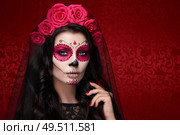 Portrait of a woman with sugar skull makeup over red background. Halloween costume and make-up. Portrait of Calavera Catrina. Стоковое фото, агентство Ingram Publishing / Фотобанк Лори