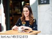 Young woman drinking coffee in an urban cafe bar. Middle-aged female sitting at table at an outside terrace. Girl with california highlights hairstyle.. Middle-aged woman drinking coffee in an urban cafe bar. Стоковое фото, агентство Ingram Publishing / Фотобанк Лори