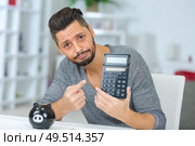 man with regretful expression holding pocket calculator and piggybank. Стоковое фото, агентство Ingram Publishing / Фотобанк Лори