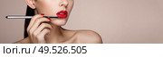 Beautiful woman paints lips with lipstick. Beautiful woman face. Makeup detail. Beauty girl with perfect skin. Red lips and nails manicure. Стоковое фото, агентство Ingram Publishing / Фотобанк Лори