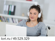 Teenage girl in wheelchair wearing headphones and using laptop. Стоковое фото, агентство Ingram Publishing / Фотобанк Лори