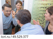 beautiful optician helping male customer choosing eye glasses. Стоковое фото, агентство Ingram Publishing / Фотобанк Лори
