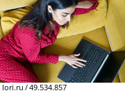 Young woman wearing pyjamas at home using laptop computer on a couch. Persian woman at home using laptop computer. Стоковое фото, агентство Ingram Publishing / Фотобанк Лори