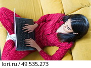 Young woman wearing pyjamas at home using laptop computer on a couch. Persian woman at home using laptop computer. Стоковое фото, агентство Ingram Publishing / Фотобанк Лори