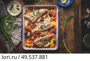 Tasty Bass fish fillets in Mediterranean sauce with tomatoes, olives and capers in baking pan on rustic wooden background with ingredients. Top view. Стоковое фото, агентство Ingram Publishing / Фотобанк Лори