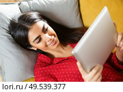 Young woman wearing pyjamas at home using digital tablet on a couch. Persian woman at home using digital tablet. Стоковое фото, агентство Ingram Publishing / Фотобанк Лори