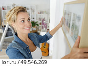 woman positioning picture frame on wall. Стоковое фото, агентство Ingram Publishing / Фотобанк Лори