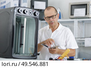 repairman using phone to fix domestic oven in kitchen. Стоковое фото, агентство Ingram Publishing / Фотобанк Лори
