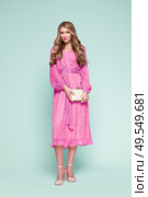 Blonde young woman in elegant pink dress. Model posing on a blue background in full length. Jewelry and hairstyle. Girl with handbag. Fashion photo. Стоковое фото, агентство Ingram Publishing / Фотобанк Лори