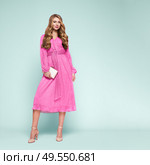 Blonde young woman in elegant pink dress. Model posing on a blue background in full length. Jewelry and hairstyle. Girl with handbag. Fashion photo. Стоковое фото, агентство Ingram Publishing / Фотобанк Лори