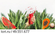 Female hand with red drink bottle: juice or smoothie leaned out of jungle  with fruits , coconut and water melon with text summer at white background. Healthy lifestyle. Summer mood. Splash. Стоковое фото, агентство Ingram Publishing / Фотобанк Лори