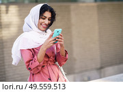 Young Arab woman wearing hijab headscarf texting message with her smartphone in urban background.. Young Arab woman wearing hijab texting message with her smartphone. Стоковое фото, агентство Ingram Publishing / Фотобанк Лори