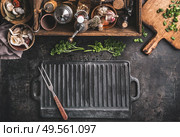 Grill or BBQ food background with empty cast iron grill griddle and meat fork  on roast rustic kitchen table. Wooden box with seasonings, oils and other kitchen utensils.Top view. Place for design. Стоковое фото, агентство Ingram Publishing / Фотобанк Лори