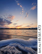 Vertical orientation, golden hour, waterscape. Lot of white fluffy foam on the shore of a pond. Surf created by the lake waves, against colorful evening sky. Idyllic scene, peaceful sunset background. Стоковое фото, агентство Ingram Publishing / Фотобанк Лори