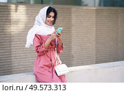 Young Arab woman wearing hijab headscarf texting message with her smartphone in urban background.. Young Muslim woman wearing hijab texting message with her smartphone. Стоковое фото, агентство Ingram Publishing / Фотобанк Лори