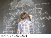 Boy with chalk writting on math formulas black board. Boy writting on black board. Стоковое фото, агентство Ingram Publishing / Фотобанк Лори
