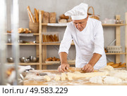 Senior male baker works with rolling pin, rolls out and spreads out pieces of dough. Стоковое фото, фотограф Яков Филимонов / Фотобанк Лори