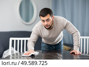 Young bachelor wiping surface of dining table in apartment. Стоковое фото, фотограф Яков Филимонов / Фотобанк Лори