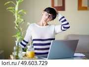 Woman teleworking from home with her laptop taking a stretch break.. Middle-aged woman teleworking taking a stretch break. Стоковое фото, агентство Ingram Publishing / Фотобанк Лори