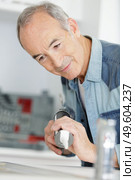senior plumber putting a silicone sealant in a kitchen. Стоковое фото, агентство Ingram Publishing / Фотобанк Лори