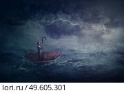 Person sailing alone the ocean on an umbrella boat, looking for shore. Surreal scene with a storm over the sea. Fantastic adventure concept. Business despair metaphor, conquering and facing adversity. Стоковое фото, агентство Ingram Publishing / Фотобанк Лори