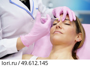 Aesthetic doctor injecting botulinum toxin into the forehead of her middle-aged patient. Facial treatment done in a cosmetic surgery clinic.. Aesthetic doctor injecting botulinum toxin into the forehead of her middle-aged patient. Стоковое фото, агентство Ingram Publishing / Фотобанк Лори