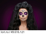 Portrait of a woman with sugar skull makeup over purple background. Halloween costume and make-up. Portrait of Calavera Catrina. Стоковое фото, агентство Ingram Publishing / Фотобанк Лори