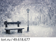 Winter time scene with a wooden bench and street lamp covered with snow under a snowfall in the park. Wonderful holiday season background, Merry Christmas magic atmosphere. Tranquil and peaceful view. Стоковое фото, агентство Ingram Publishing / Фотобанк Лори