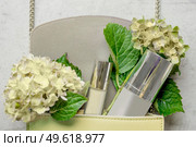 Pale yellow handbag with cosmetic bottle, lipgloss and hydrangea flowers on white wooden background. Feminine lifestyle concept. Top view. Стоковое фото, агентство Ingram Publishing / Фотобанк Лори