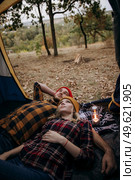 Young couple a guy and a girl in bright knitted hats stopped at a camping near the fire. Стоковое фото, агентство Ingram Publishing / Фотобанк Лори