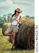 girl with black hair in beige wool coats and suspenders stands near the haystacks. Стоковое фото, агентство Ingram Publishing / Фотобанк Лори