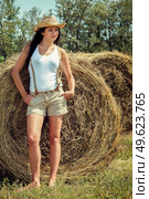 girl with black hair in beige wool coats and suspenders stands near the haystacks. Стоковое фото, агентство Ingram Publishing / Фотобанк Лори
