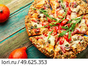 Pizza with salami, cheese, tomato on a pumpkin flatbread. Autumn recipe. Pumpkin-based pizza, wooden table. Стоковое фото, агентство Ingram Publishing / Фотобанк Лори