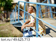 Beautiful young black woman combed with colorful braids sitting on an urban bridge with a camera on vacation.. Young black woman combed with braids sitting on an urban bridge with a camera on vacation. Стоковое фото, агентство Ingram Publishing / Фотобанк Лори