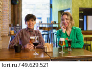 Happy adult women in casual clothes smiling and enjoying alcohol drinks while sitting at table during friends meeting on weekend day in pub. Cheerful girlfriends sitting at table in bar. Стоковое фото, агентство Ingram Publishing / Фотобанк Лори