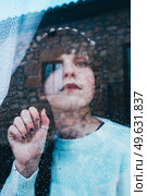 Sad woman alone in her home looking through a window in a rainy day. Стоковое фото, агентство Ingram Publishing / Фотобанк Лори