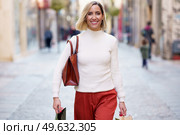 Positive female shopaholic with handbag carrying paper bags with purchases after shopping in stores and smiling at camera. Smiling woman with shopping bags walking on street. Стоковое фото, агентство Ingram Publishing / Фотобанк Лори