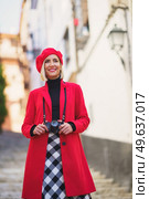 Low angle of happy young lady with blond hair, in stylish warm clothes and beret, smiling and looking away while admiring and photographing town on camera. Smiling female tourist with photo camera standing on stairs on city street. Стоковое фото, агентство Ingram Publishing / Фотобанк Лори